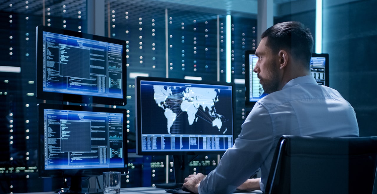 A person at a workstation with several computer screens displaying maps and data.