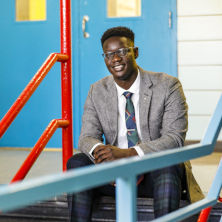 Edmund Adjapong in a gray suit sitting on stairs posing