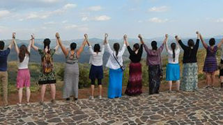 Students joining hands as they look at a large vista. 