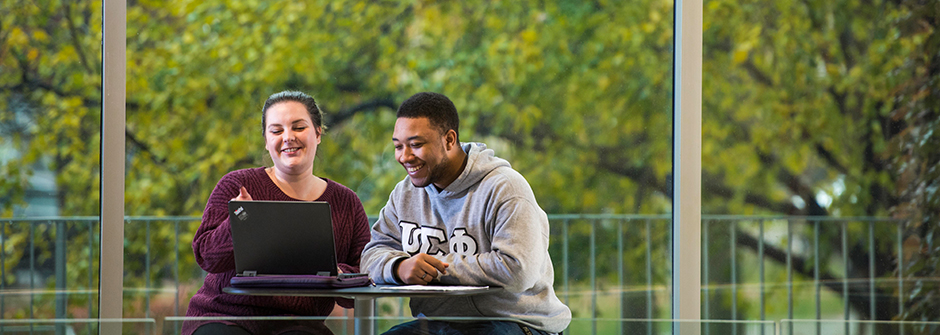 Two Seton Hall students in Jubilee Hall having a conversation while looking at a laptop.