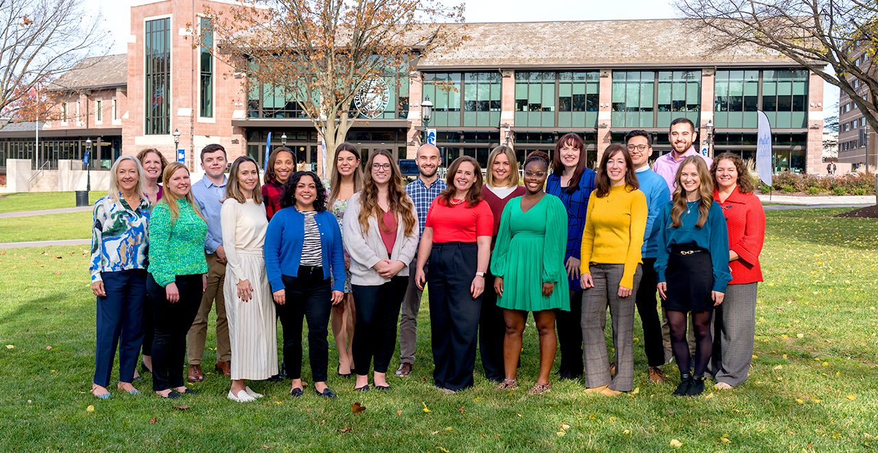 A photo of the admissions counselors team holding a Welcome to Seton Hall sign on the University Green. 