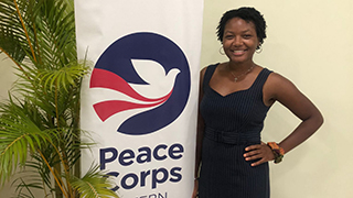 Alumna Tajah McCray standing next to a Peace Corps poster