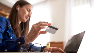 Person holding a credit card in front of an open laptop.