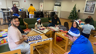 Students sitting in DOVE's headquarters wearing santa hats and wrapping presents. 