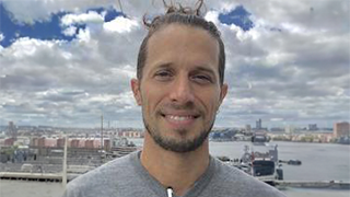 Graham Burnett with a beard smiling in front of a cityscape