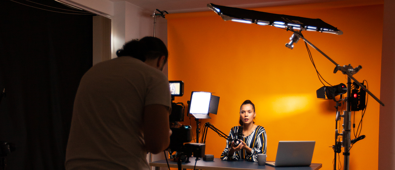 A photo of a recording set with someone filming a person seated at a table.