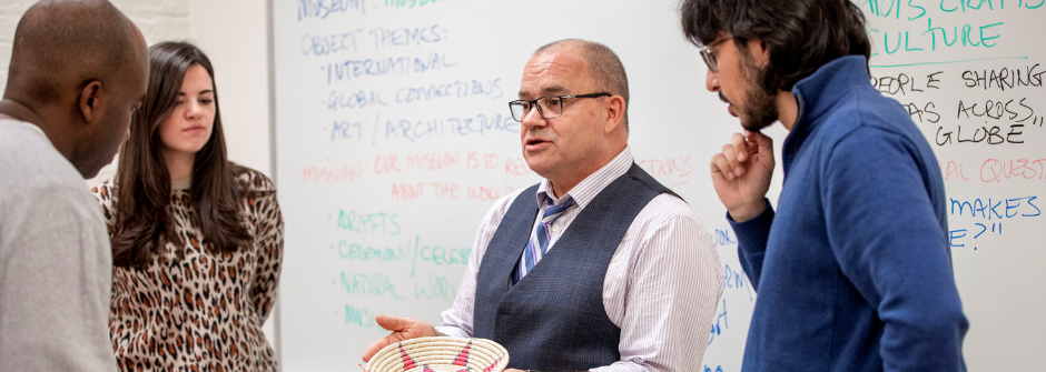 Image of 3 museum professions students gathering around a professor. 