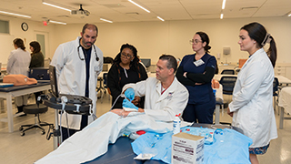 A group of nursing students surrounding an instructor and a mannakin. 