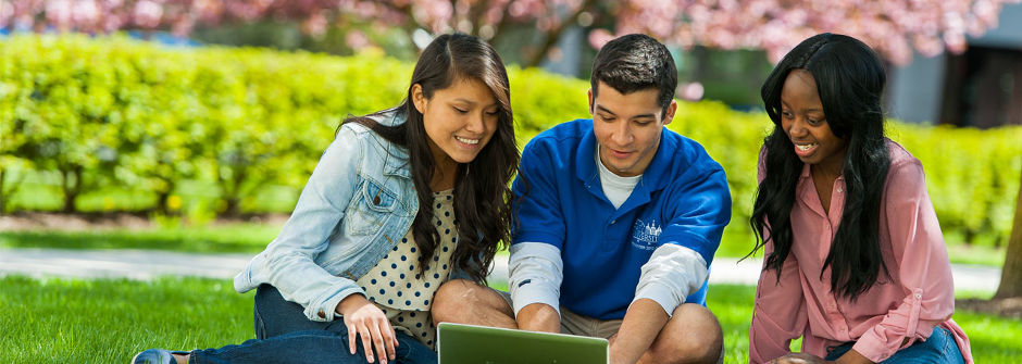 Students looking at a laptop on the grass. 